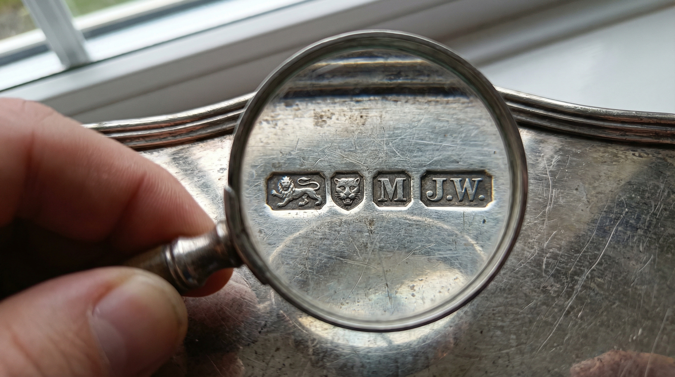 close-up of silver hallmarks being examined with magnifying glass